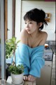 A woman in a blue sweater sitting next to a potted plant.